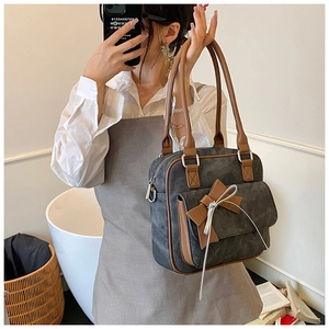 Detail of grey suede shoulder bag with brown leather handles and a bow decoration