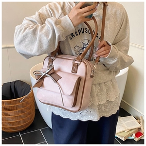 Close-up of pink and brown leather shoulder bag with decorative bow and flap pocket