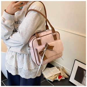 Detail of pink suede bag featuring brown bow accent and silver ring hardware