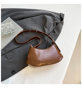 Detail view of brown crescent shoulder bag with smooth texture on a grey blazer