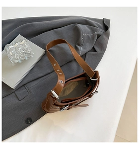 Close-up of deep brown leather shoulder bag with adjustable silver eyelet strap and buckle