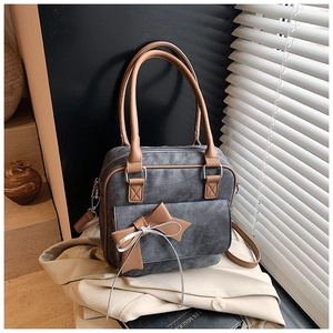 Detail of grey denim tote bag featuring brown faux leather handles and a large bow decor
