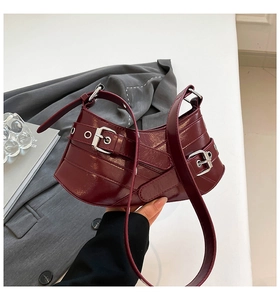Detail of burgundy glossy leather handbag with multiple silver buckles and strap decoration