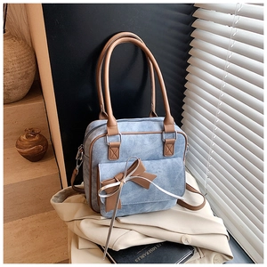 Close-up of light blue textured handbag featuring brown leather trim and bow detail