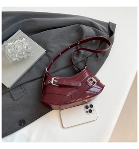 Detailed view of dark burgundy glossy leather bag with decorative buckles and adjustable strap