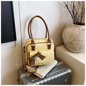Detail of light yellow underarm bag with brown bow accent and silver ribbon on travel case