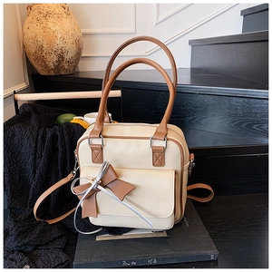 Detail shot of beige shoulder bag showing the large front pocket and double bow decoration