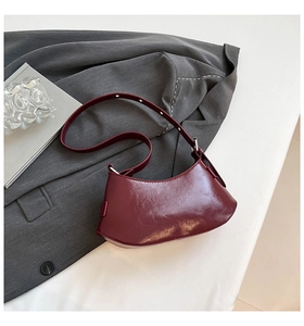 Close-up of a burgundy leather crescent bag with glossy texture and silver hardware
