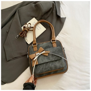 Detail of grey canvas tote bag with brown leather trim and bow accent on white fabric