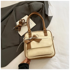 Close-up of beige underarm bag with caramel trim, bow detail and silver metal hardware