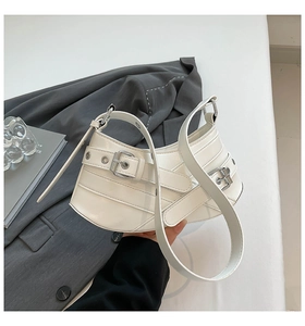Detail of white half-moon bag with silver buckles and metal eyelets on shoulder strap