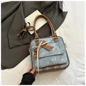 Close-up of light blue denim shoulder bag with brown leather bow and strap details