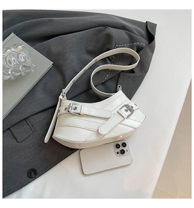 Detailed view of white Y2K motorcycle shoulder bag with metal buckles and phone for scale