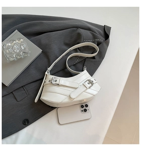 Detail shot of white saddle bag showing layered design and silver buckles on grey fabric