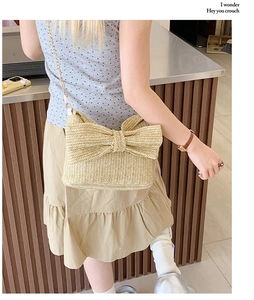 Detail of straw woven crossbody bag with a large bow and gold metal chain strap