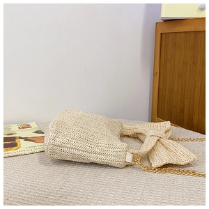 Detail of cream straw crossbody bag featuring a woven bow and golden metal chain strap