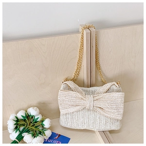 Close-up of woven straw handbag with large bow detail and gold chain on wooden backdrop