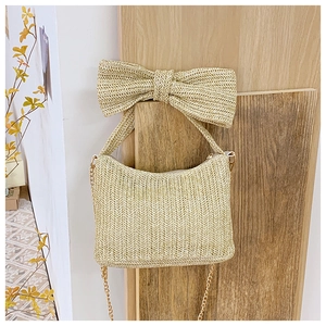Detail of beige straw tote bag with oversized bow handle and elegant gold chain strap
