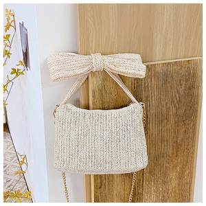 Detail of cream straw handbag featuring a large bow and gold chain on wooden wall