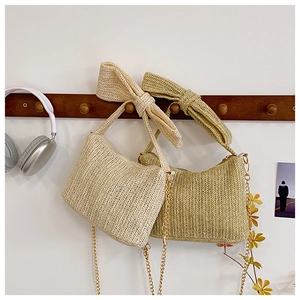 Detail of hand-woven straw crossbody bag featuring wide bow straps and golden metal chain