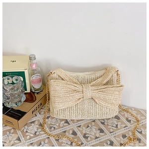 Detail of beige woven straw bag with decorative bow and gold metal chain strap