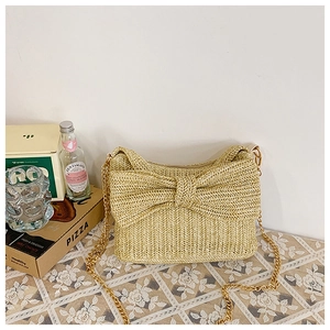 Close-up of beige straw crossbody bag with large bow decoration and gold chain strap
