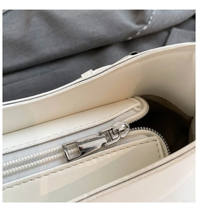 Detail shot of the silver metal zipper and glossy white leather on a stylish handbag