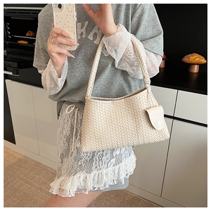 Detail of cream woven shoulder bag featuring intricate Intrecciato texture and matching charm