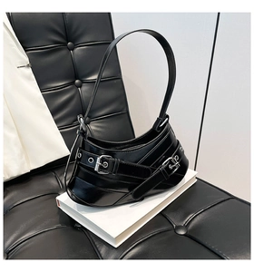 Detailed view of black patent leather baguette bag with silver buckles and curved bottom