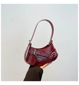 Close-up of deep red crescent shoulder bag with silver eyelets and buckle straps