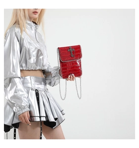 Détail du sac rouge croco avec croix gothique et chaîne argentée porté par un mannequin