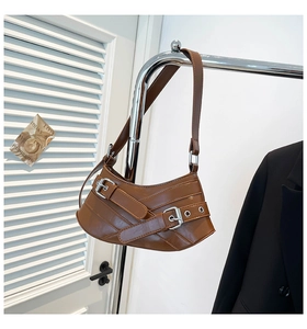 Detail of brown leather shoulder bag featuring retro buckle straps and silver eyelets