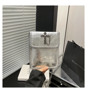 Détail du sac argenté motif crocodile avec bordure chaîne et pendentif croix gothique