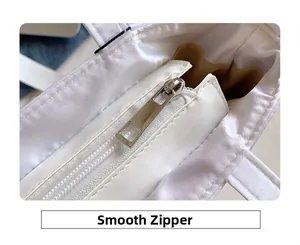 Macro view of smooth silver metal zipper and satin fabric texture on white shoulder bag