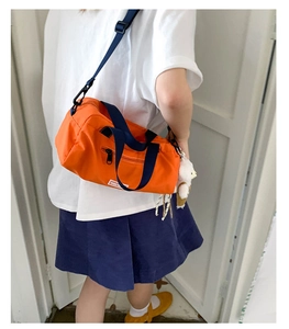 Dettaglio di una borsa sportiva in nylon arancione con spalline blu scuro e un peluche
