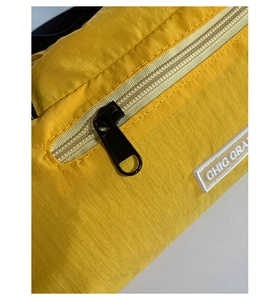 Dettaglio del tessuto nylon ripstop giallo con patch CHIC GRA e cerniera in metallo nero
