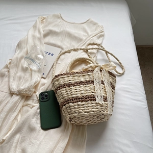 Handwoven straw bucket bag with brown stripes, white lace bow, and crossbody strap