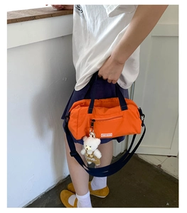 Detail of orange nylon tote bag with navy blue handles and white plush bear charm accessory
