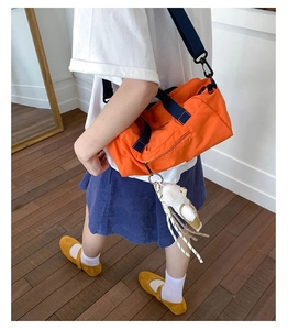 Detail of orange canvas cylinder bag with navy straps and cute white teddy bear charm