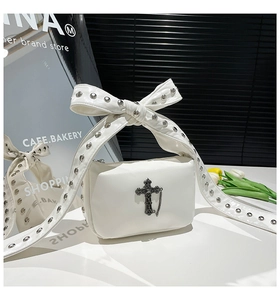 Détail du sac blanc avec bandoulière à nœud riveté et pendentif de croix gothique