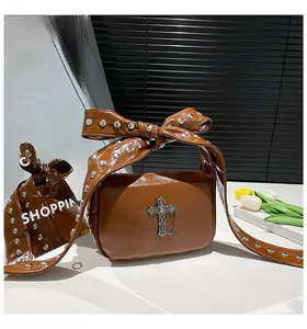 Détail du sac en cuir verni marron avec anse nœud rivetée et croix gothique argentée