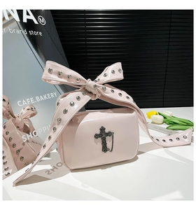Détail du sac à main en cuir verni rose avec poignée à nœud clouté et pendentif croix gothique