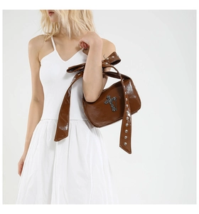 Détail du sac en cuir marron avec rivets punk et grand nœud sur la bandoulière