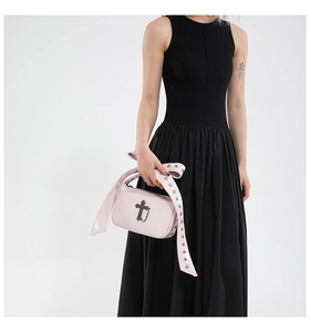 Détail du sac gothique en cuir verni rose clair avec croix en métal et rubans à œillets