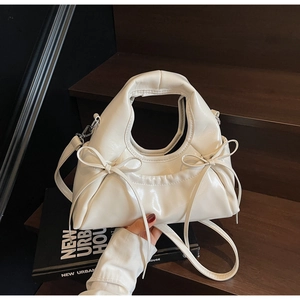 Detail of a creamy white dumpling crossbody bag with elegant bow knots on a wooden step