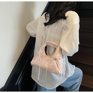 Close-up of pink glossy patent leather crossbody bag with delicate bow and pleats