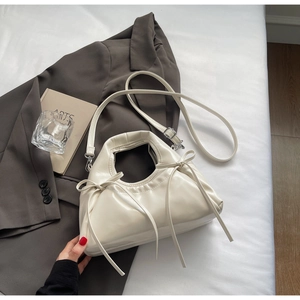 Detail of creamy white pleated leather bag with delicate bow accents on urban background