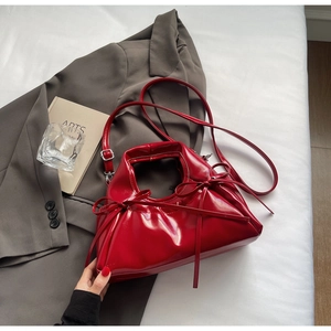 Detail of red patent leather crossbody bag with bow decoration on a gray suit background