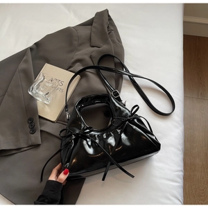 Detail of a black glossy handbag with bow decoration and adjustable strap on a gray blazer