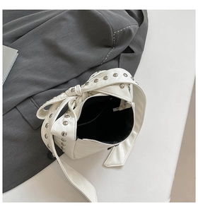 Détail du sac bandoulière en cuir blanc avec clous argentés et nœud sur la sangle